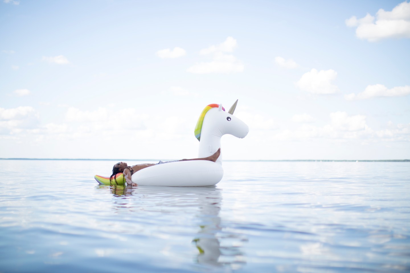 "Young man lying back on inflatable unicorn in sea, Santa Rosa Beach, Florida, USA"