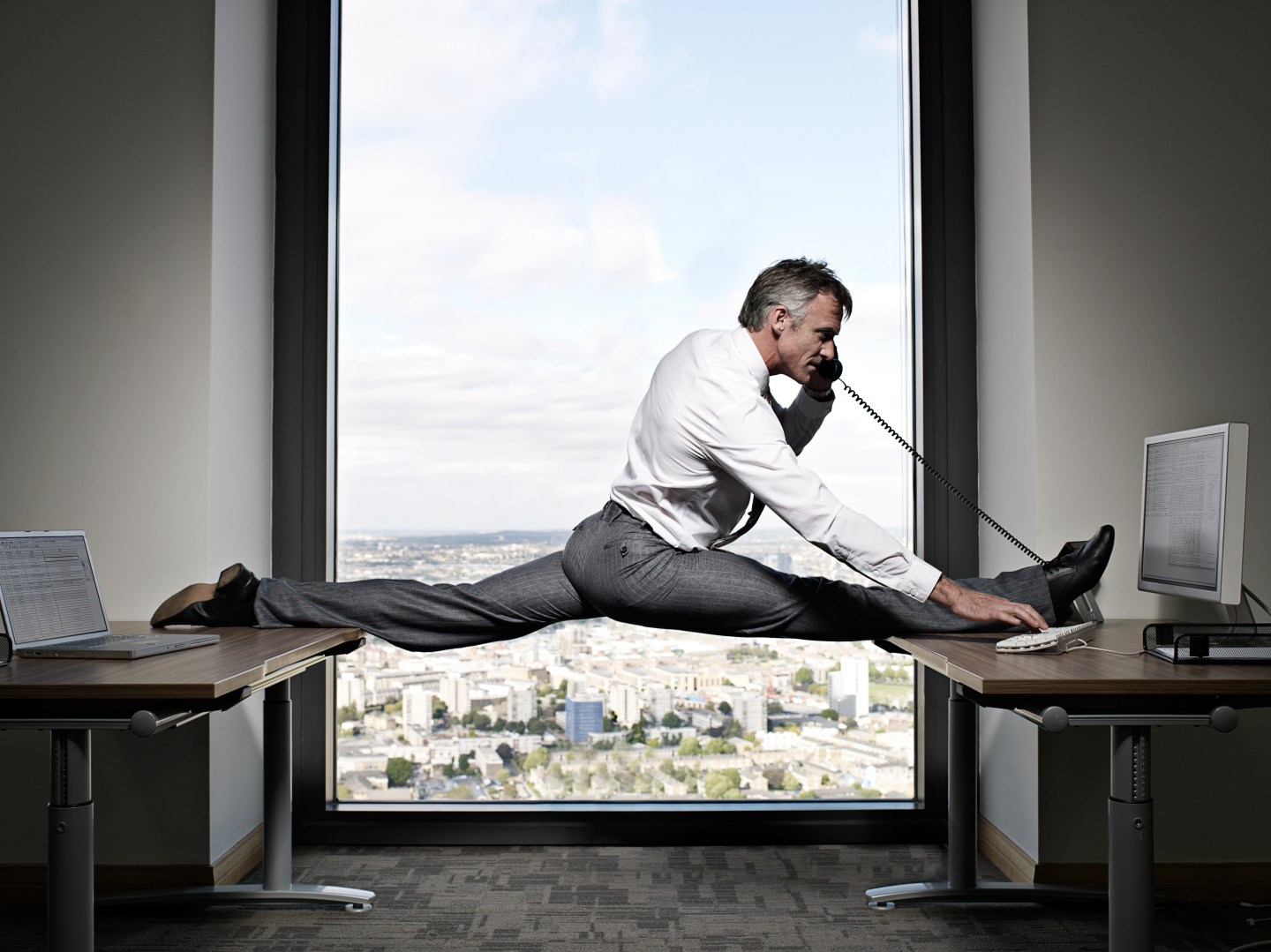 Flexible businessman balancing between two desks