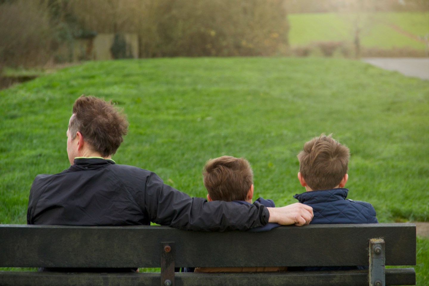 Father And Two Sons Sat On Bench In Countryside