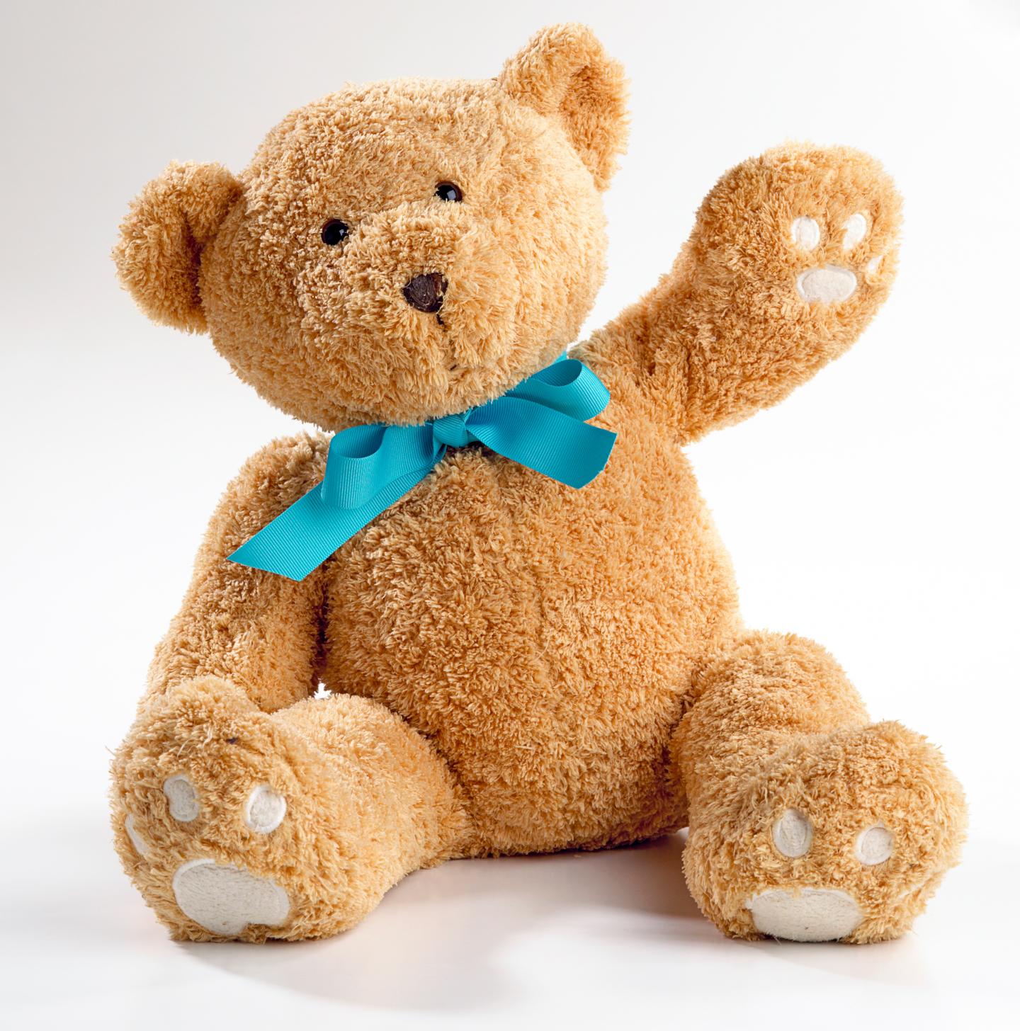Teddy bear with a blue ribbon bow holding paw in the air