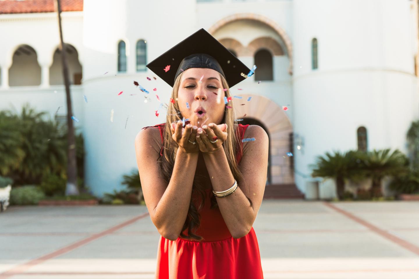 Female graduate blowing confetti from hands
