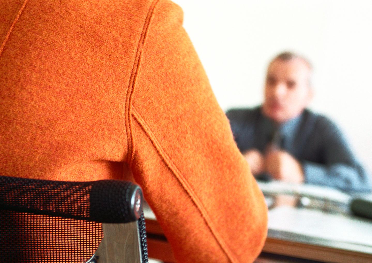 Businessman sitting at table blurred in distance, person's back in foreground.