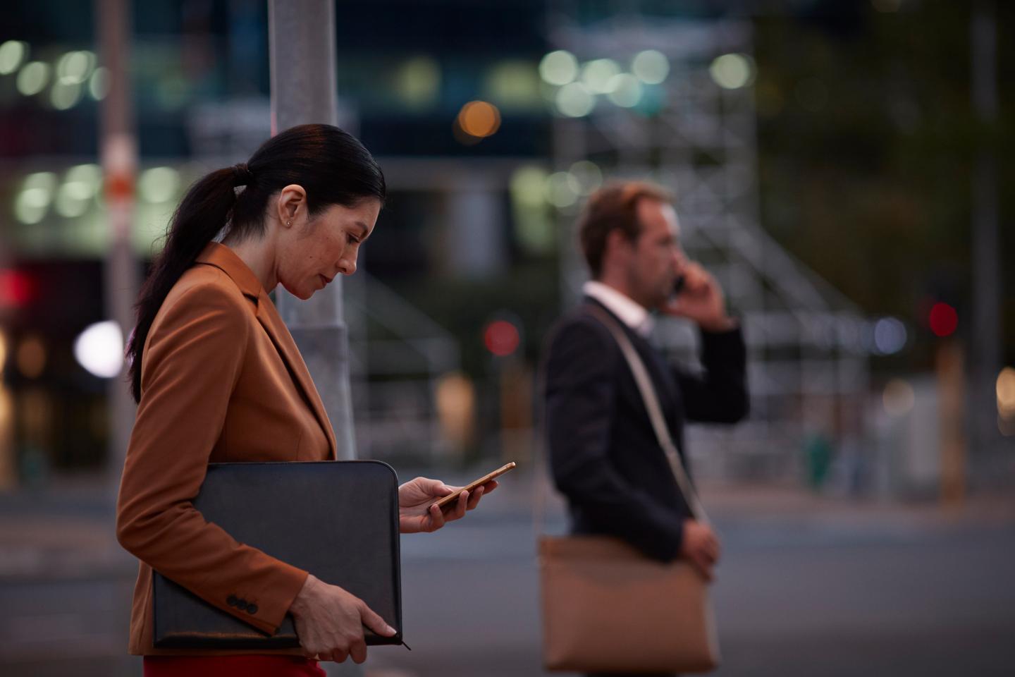 Businesswoman on street looking at phone, at night