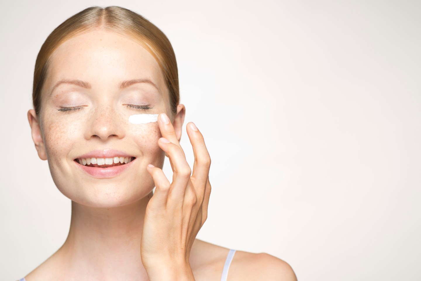 Young woman applying mositurizer under eye