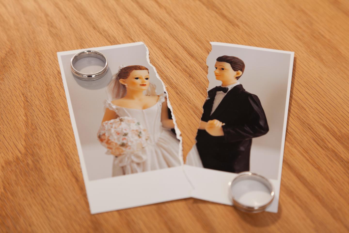 Studio shot of photo of bride and groom figurines torn in half and wedding rings