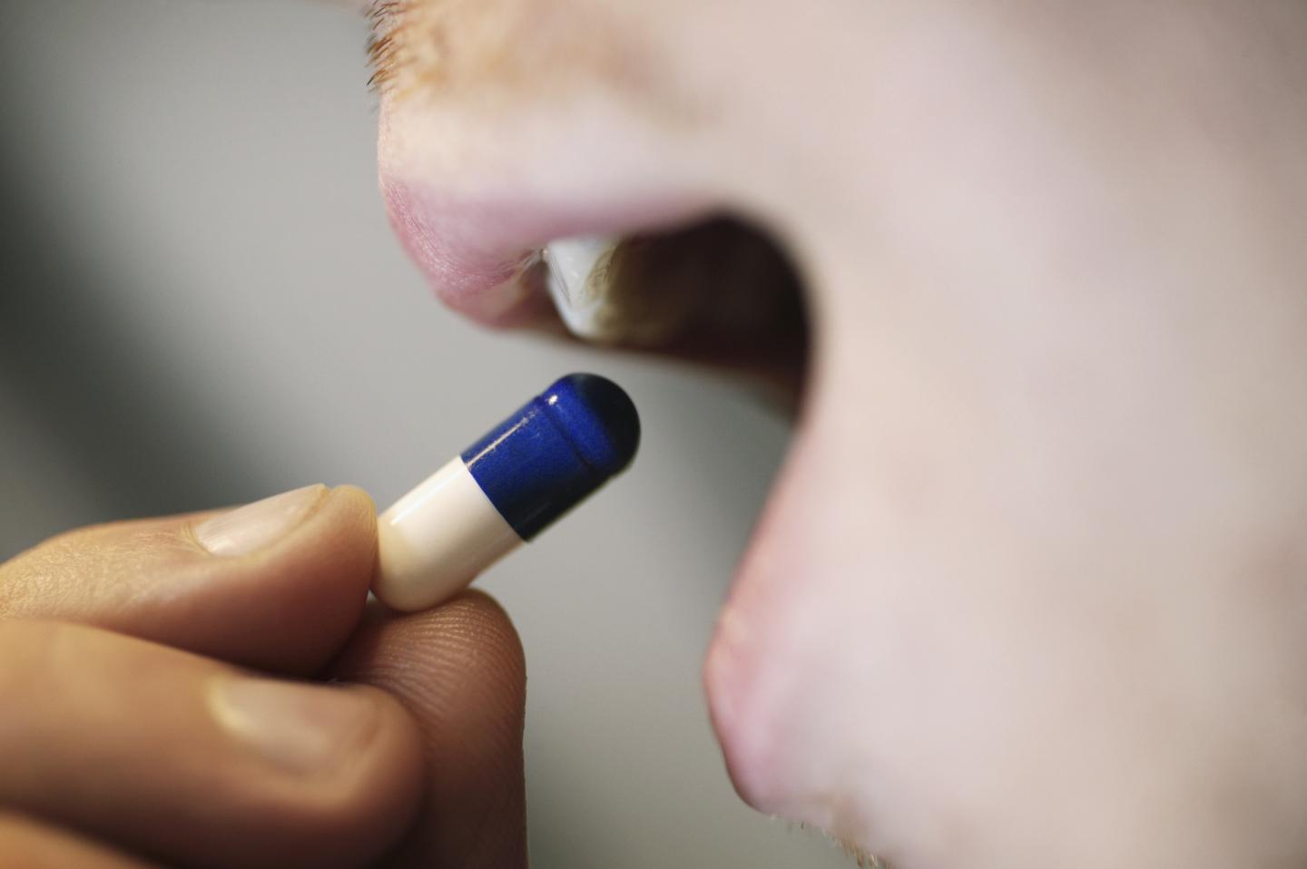 Close-up of young man placing blue and white tablet into mouth
