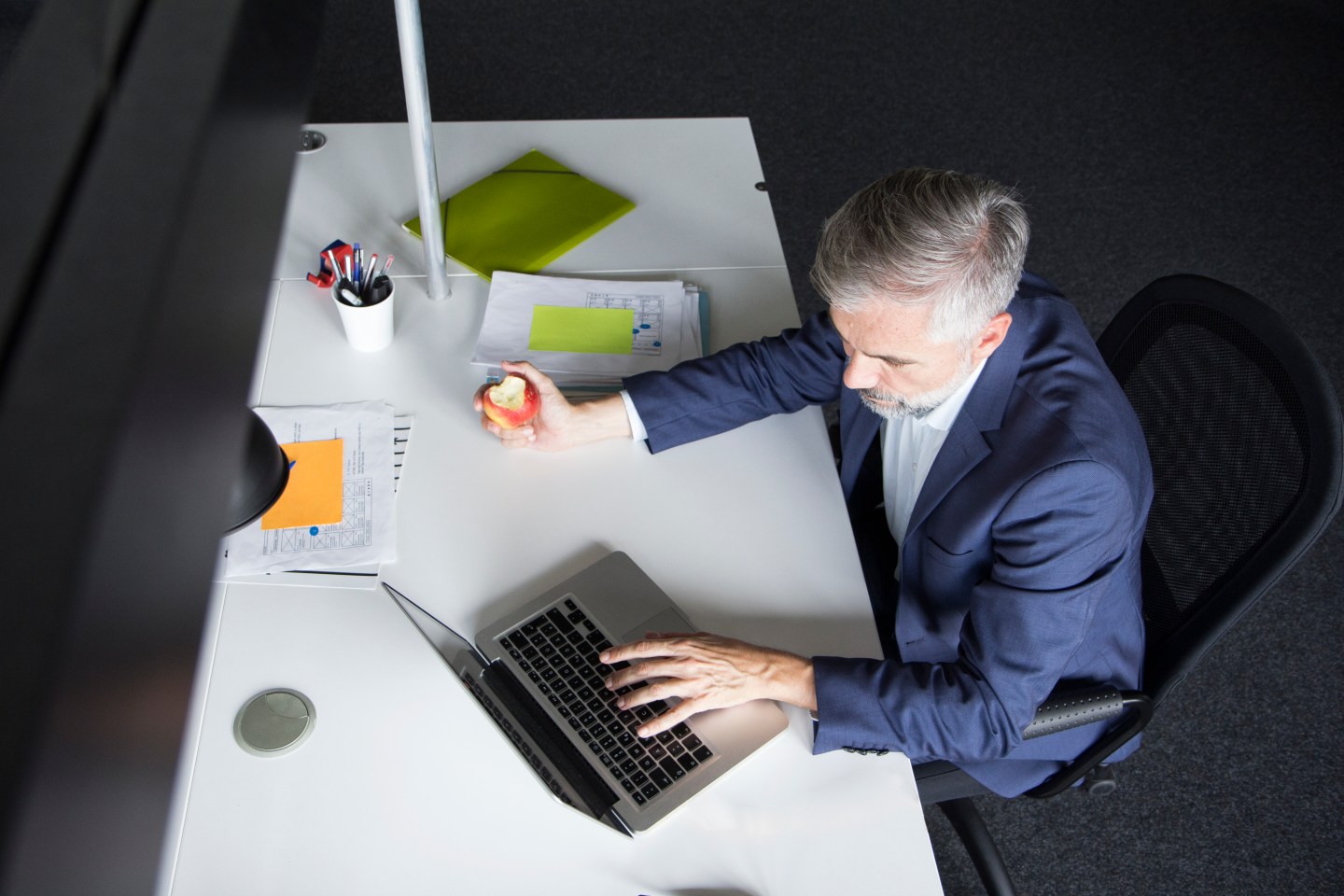 Businessman using laptop and eating an apple at office desk