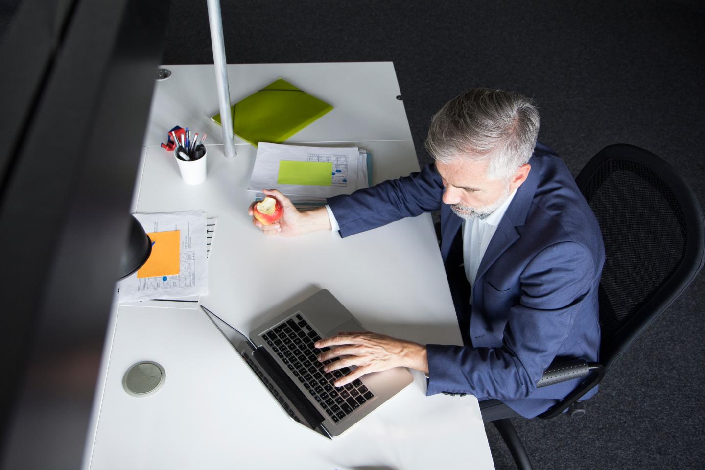 Businessman using laptop and eating an apple at office desk