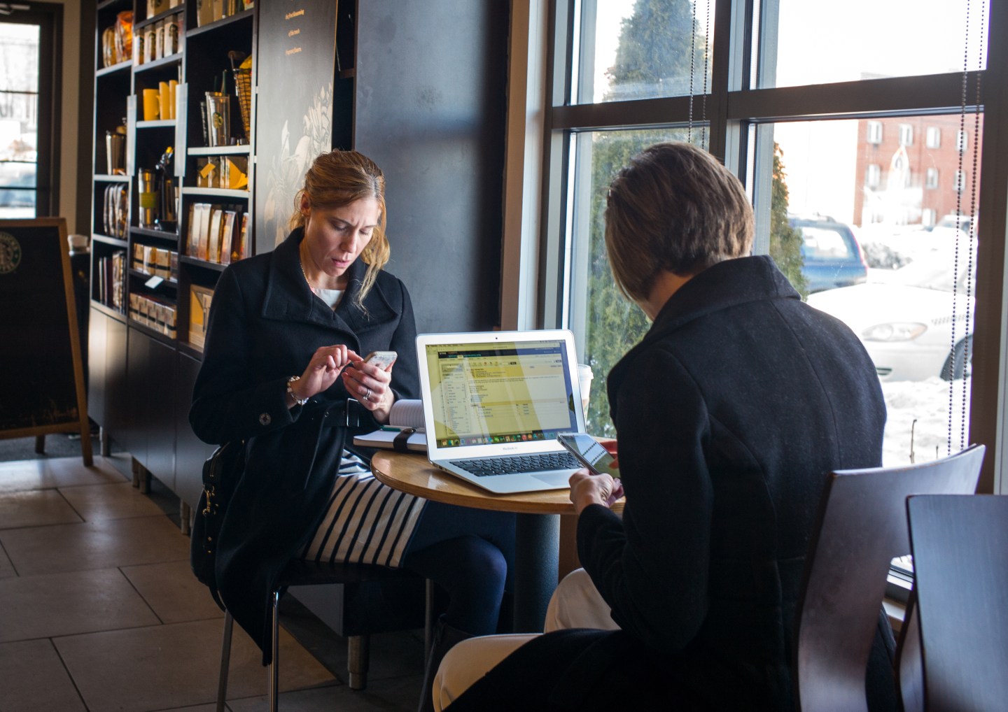 Two smartphone users working at a coffee shop.
