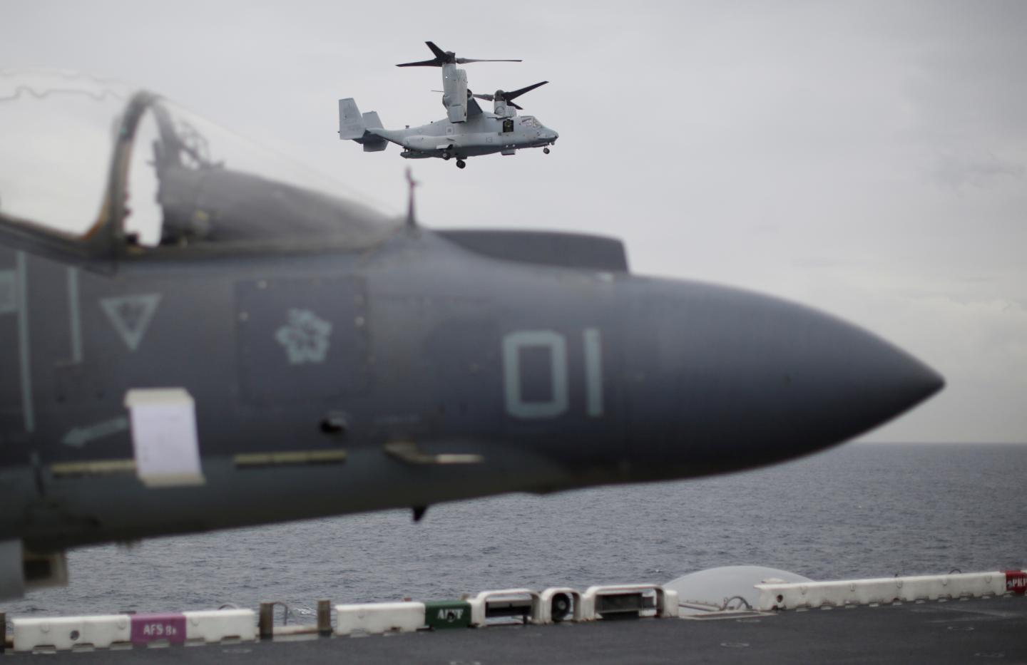 A U.S. Marines MV-22 Osprey Aircraft flies over a jet before landing on the deck of the USS Bonhomme Richard amphibious assault ship off the coast of Sydney