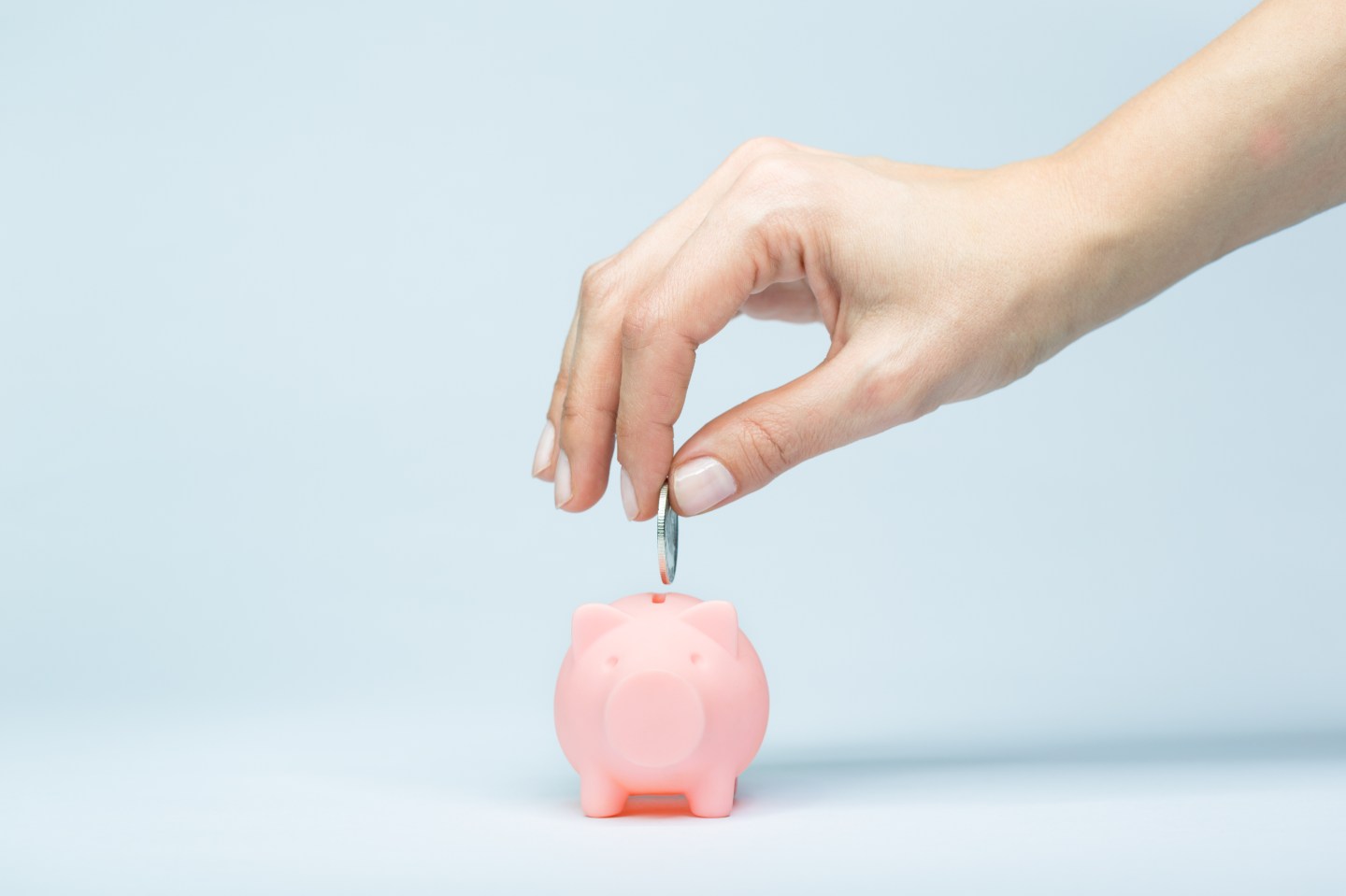 Female hand putting a coin into piggy bank