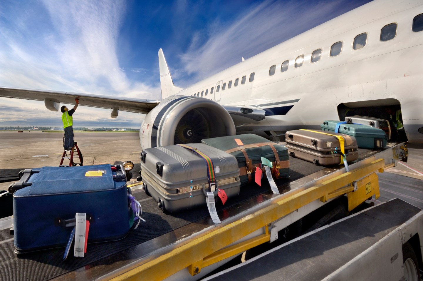 Worker checking wing as luggage rolls onto airplane