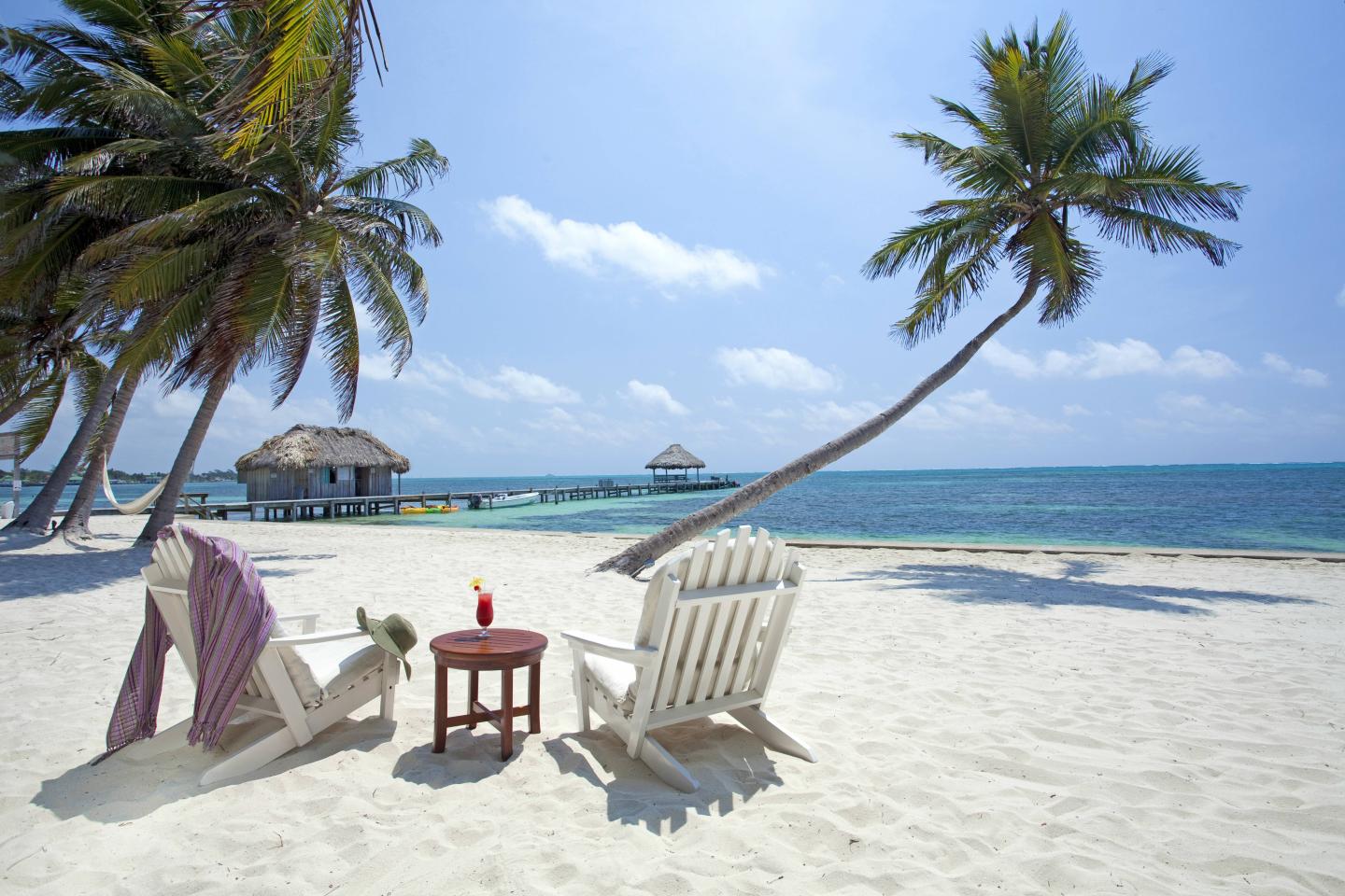Belize, Ambergris Caye, San Pedro, sun loungers on beach with coconut palms and Caribbean sea