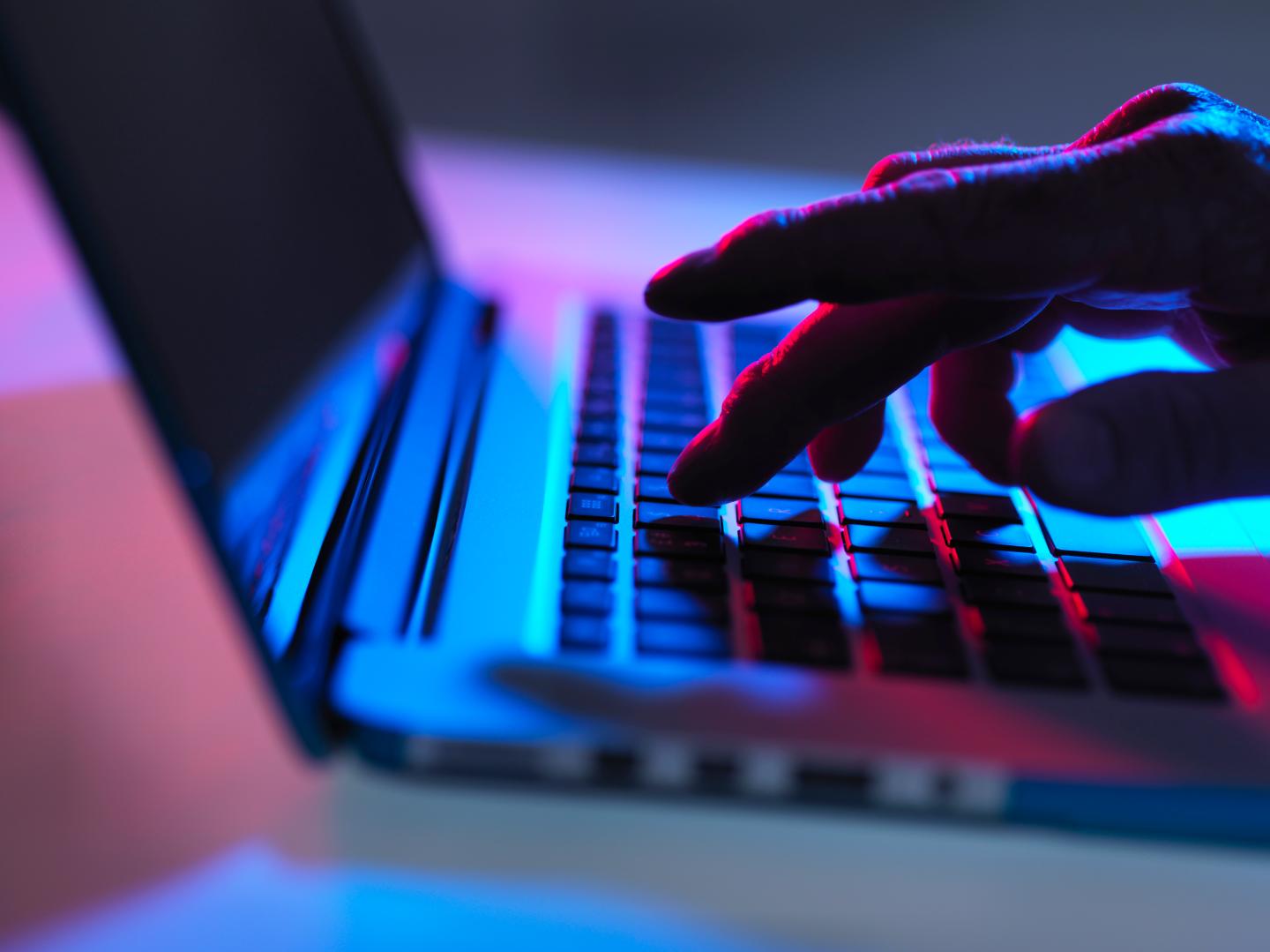 Silhouette of male hand typing on laptop keyboard at night