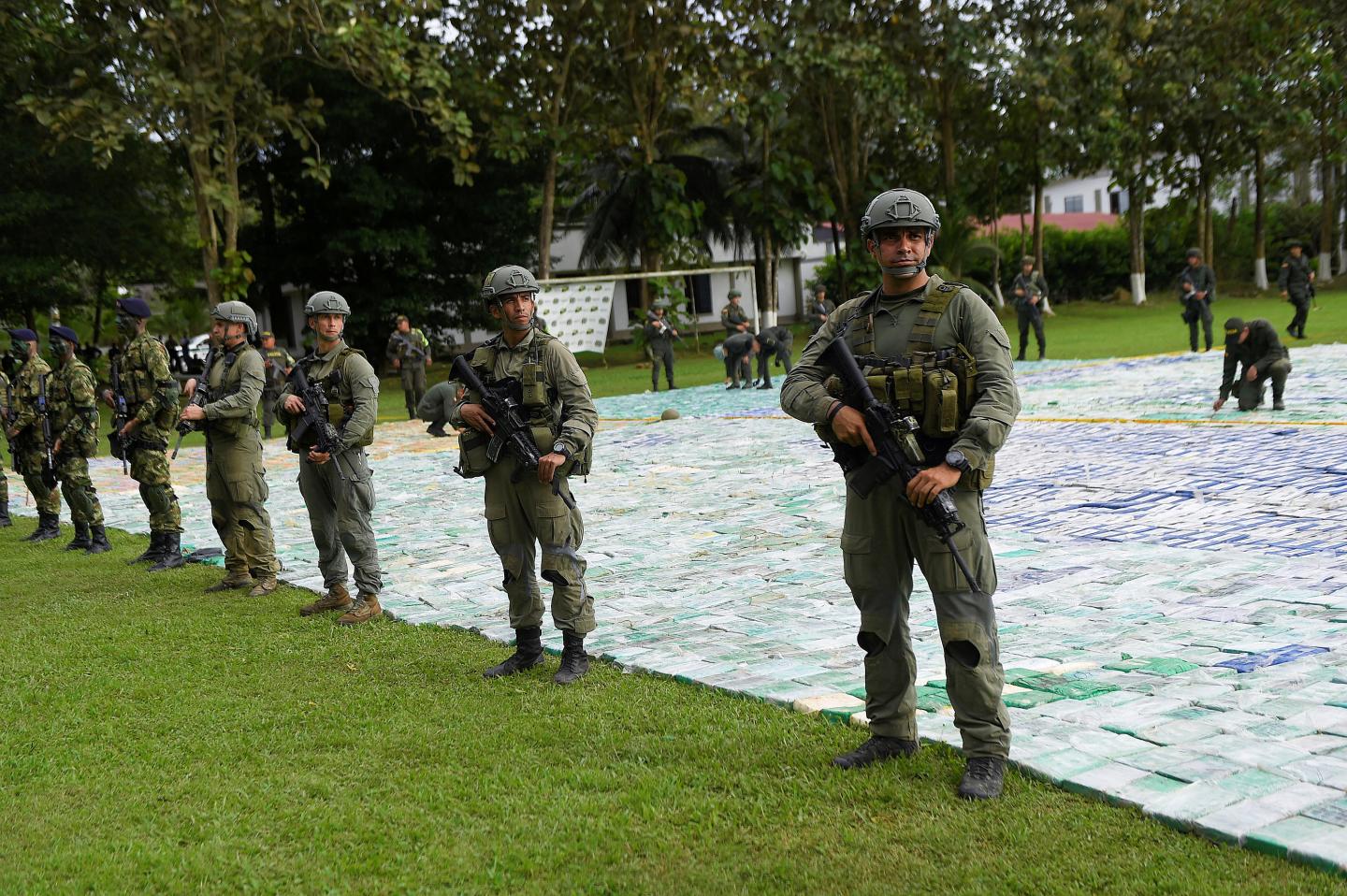 Colombian police and soldiers stand guard over more than 12 tons of cocaine laid out on grass in Apartado, Colombia