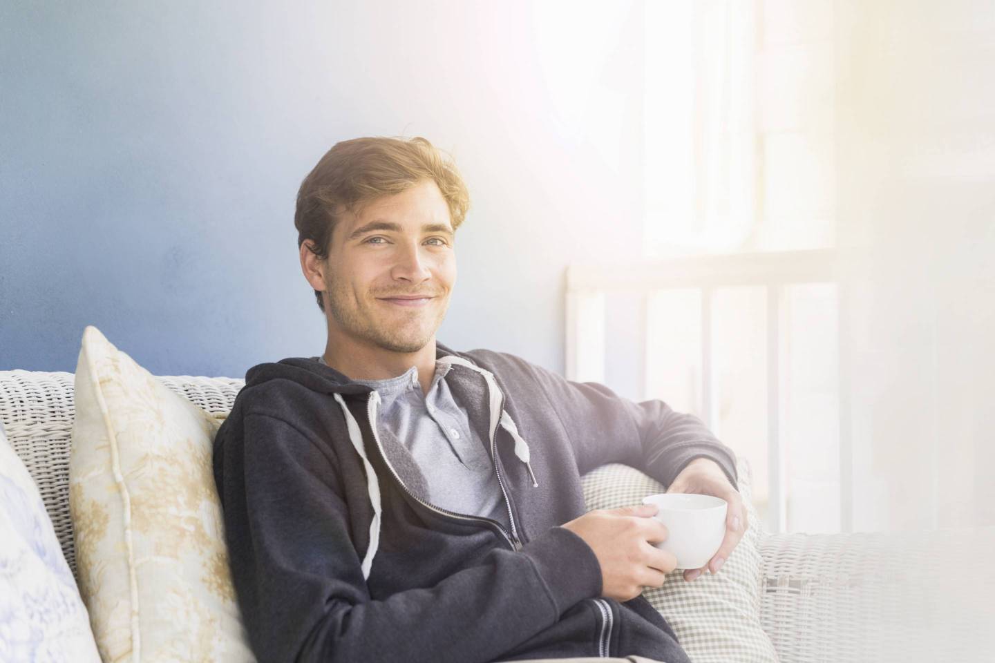 Young man holding coffee cup while sitting on sofa