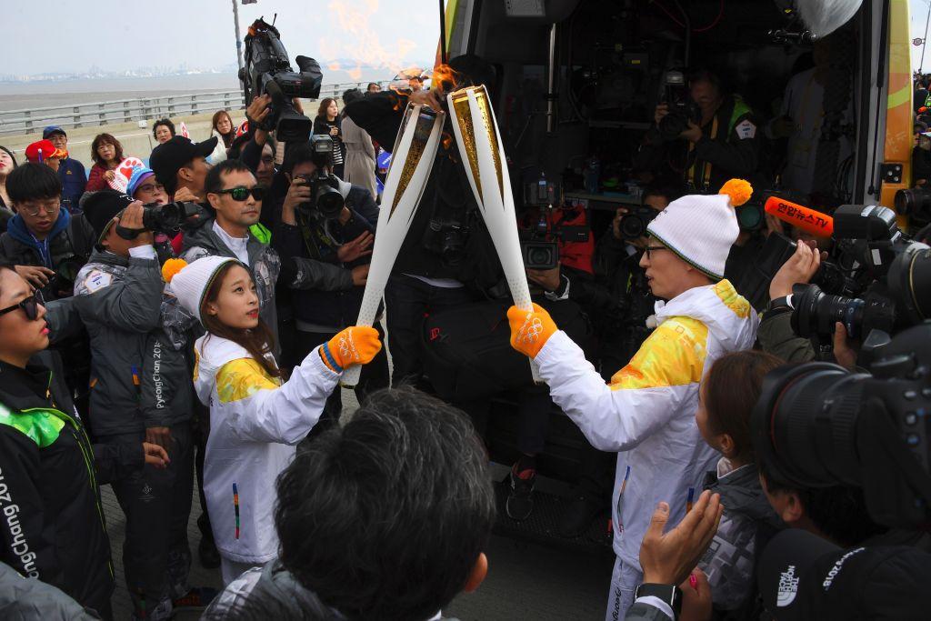Wearing stocking hate and mittens, South Korean figure skater You Young (L) passes the Olympic flame to South Korean comedian Yoo Jae-Suk.