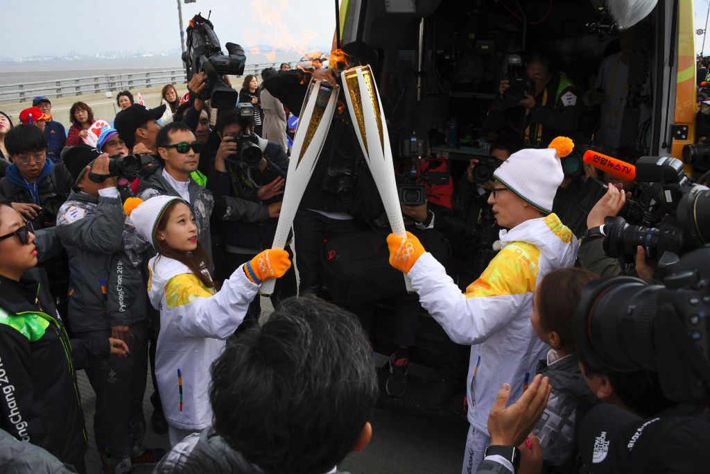 Wearing stocking hate and mittens, South Korean figure skater You Young (L) passes the Olympic flame to South Korean comedian Yoo Jae-Suk.