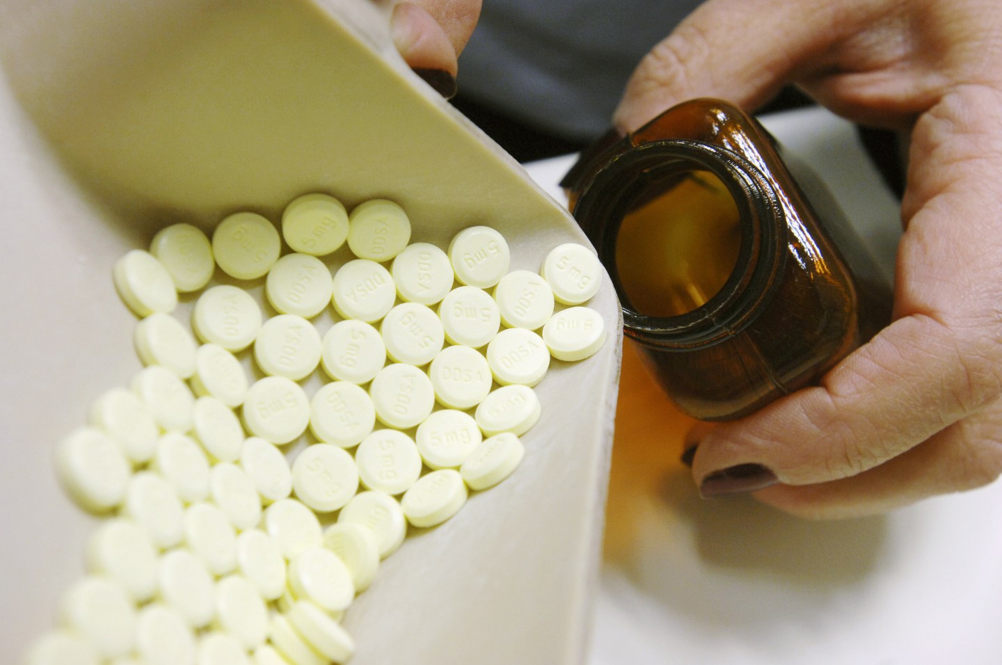 Close-up of pharmacist dispensing diazepam tablets into pill bottle