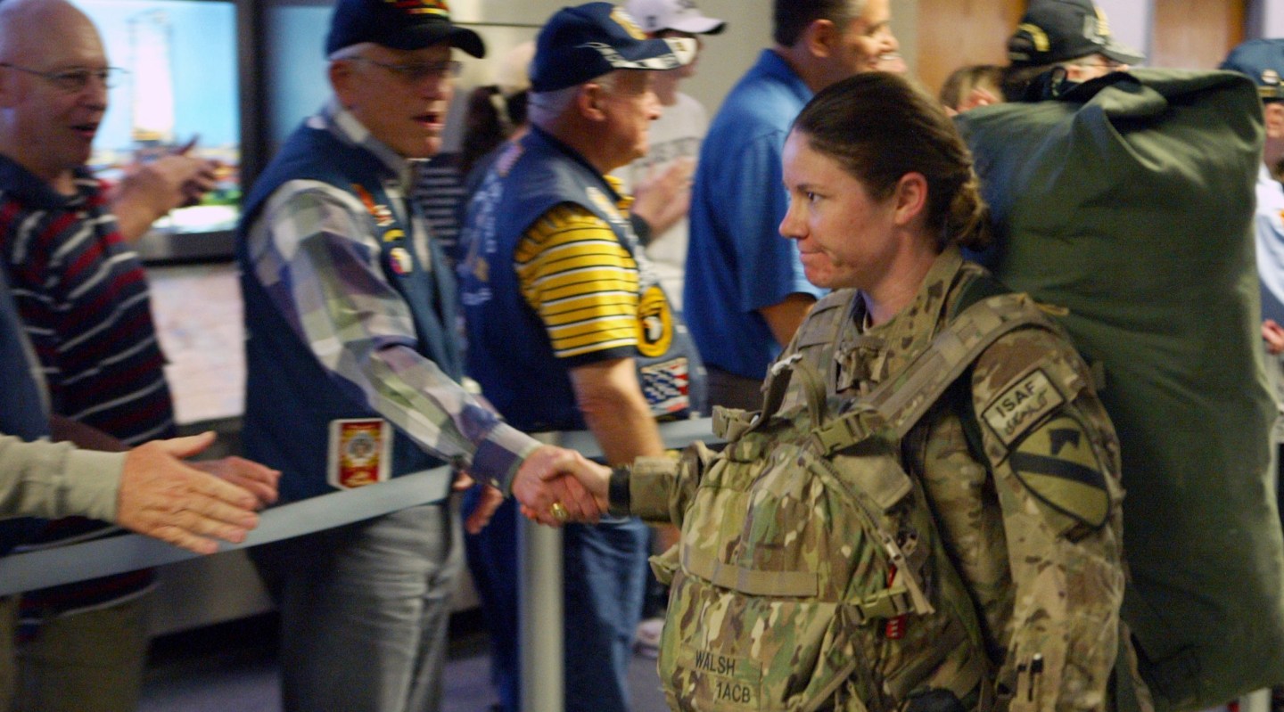 Female soldier shakes hands with older veteran onlookers at DFW International Airport
