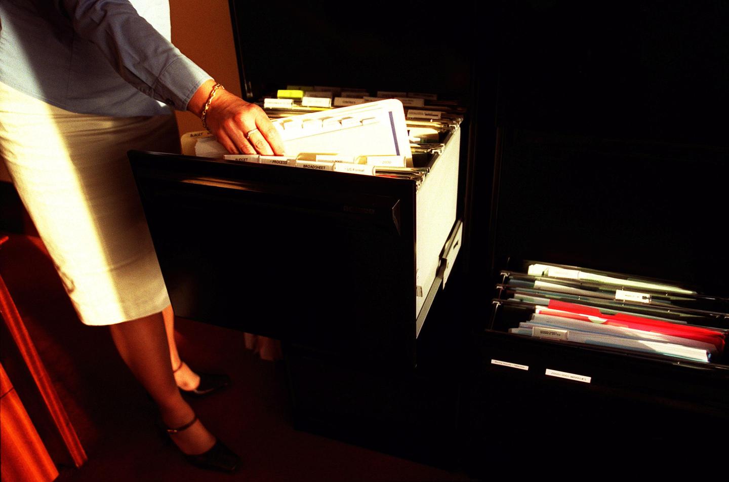 Generic woman taking files out of a filing cabinet in an office, 16 April 2002.