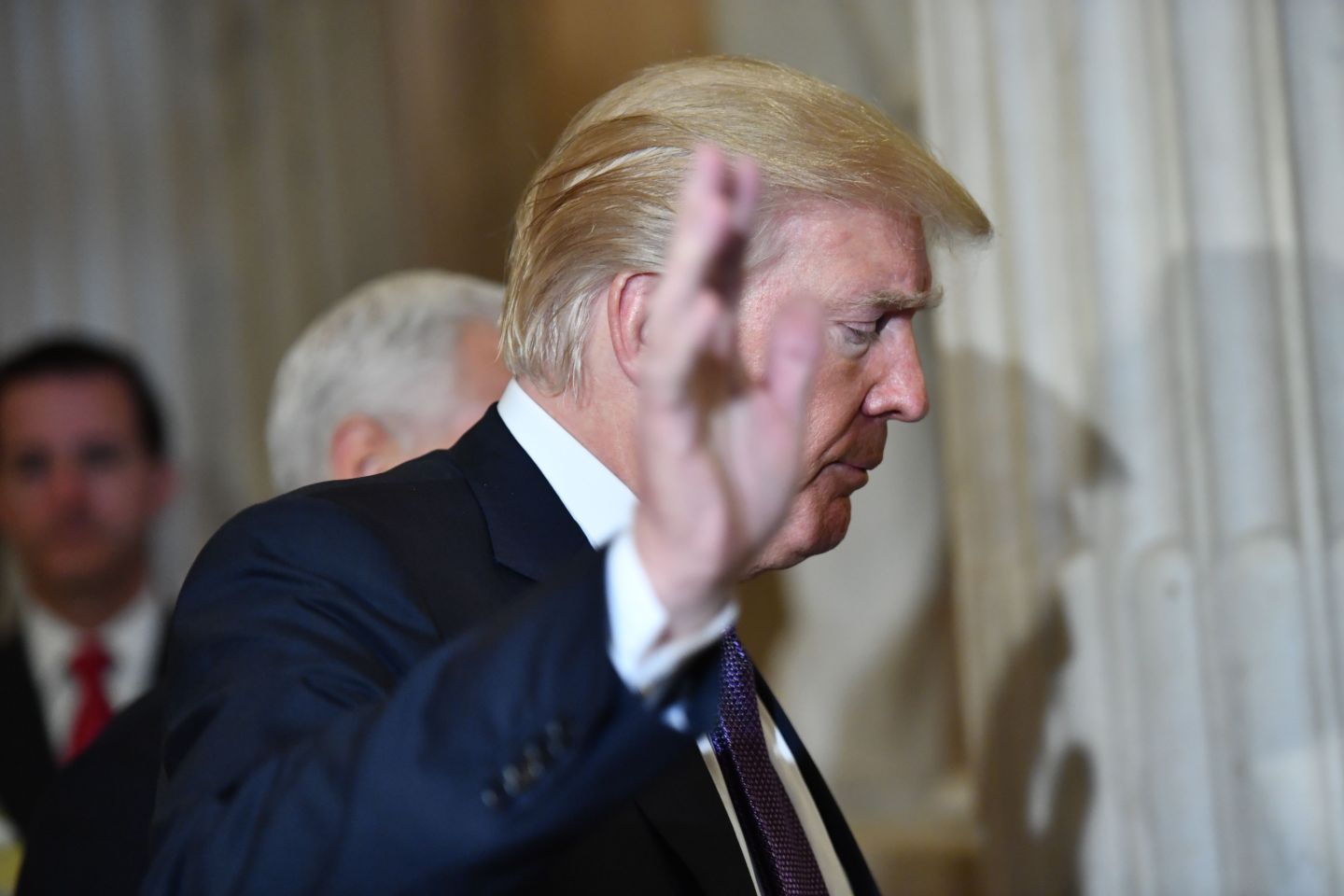 Donald Trump faces right and raises his right hand in a dismissive gesture.