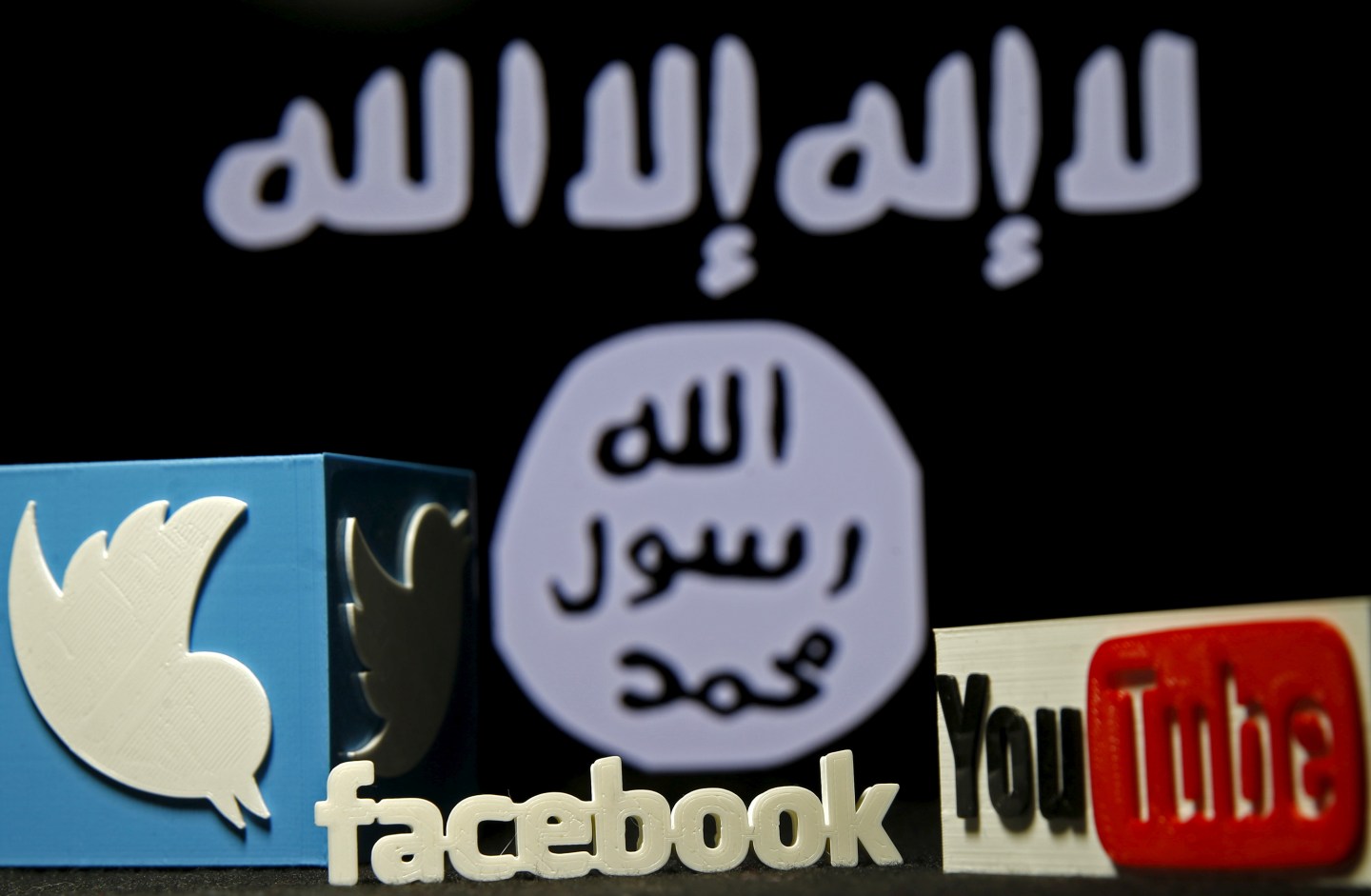 3D plastic representations of the Twitter, Facebook and Youtube logos are seen in front of a displayed ISIS flag in this photo illustration