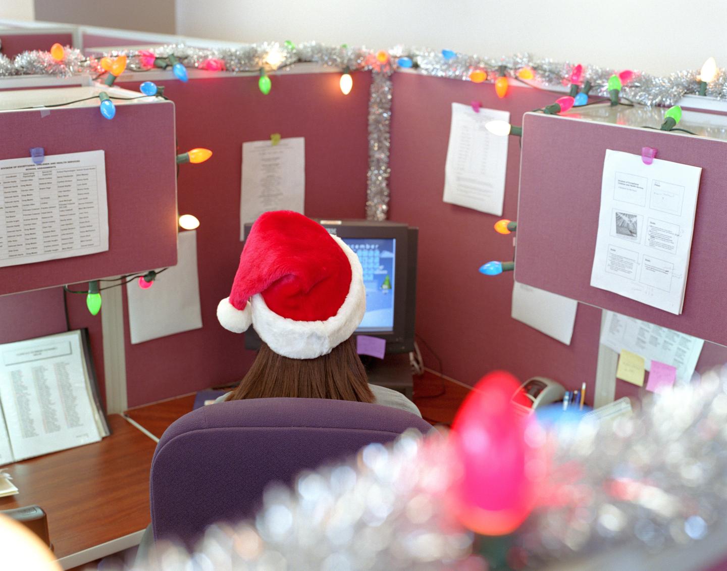 Woman working in office cubicle, wearing Santa cap, rear view