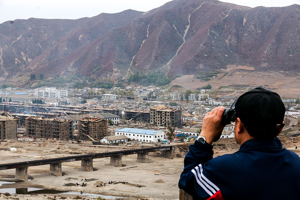 TUMEN, CHINA - 2016/10/21: Through a telescope, a Chinese tourist overlooks the North Korean people rebuilding houses in Namyang city.  At the end of August, big floods of Dooman river destroyed most of the houses of Namyang city. Namyang is a town opposite to the city of Tumen in the Chinese bank of the Tumen river. (Photo by Zhang Peng/LightRocket via Getty Images)