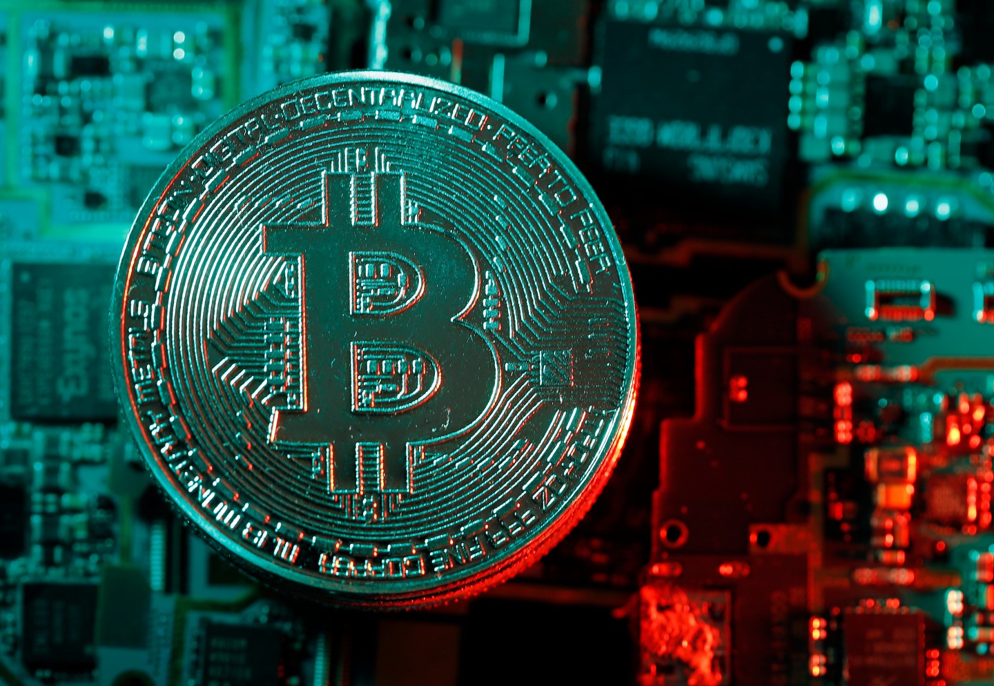 A blue and red photo with a physical coin bearing the logo of the digital cryptocurrency Bitcoin.