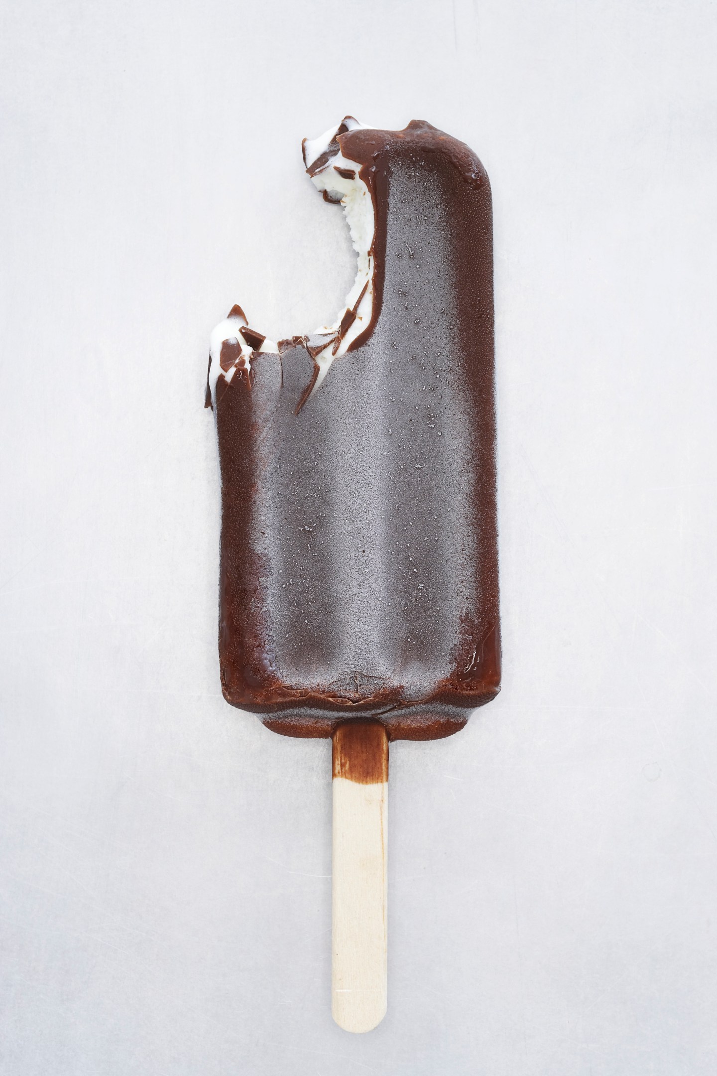 Chocolate coated ice cream on lolly stick, bite missing, close-up