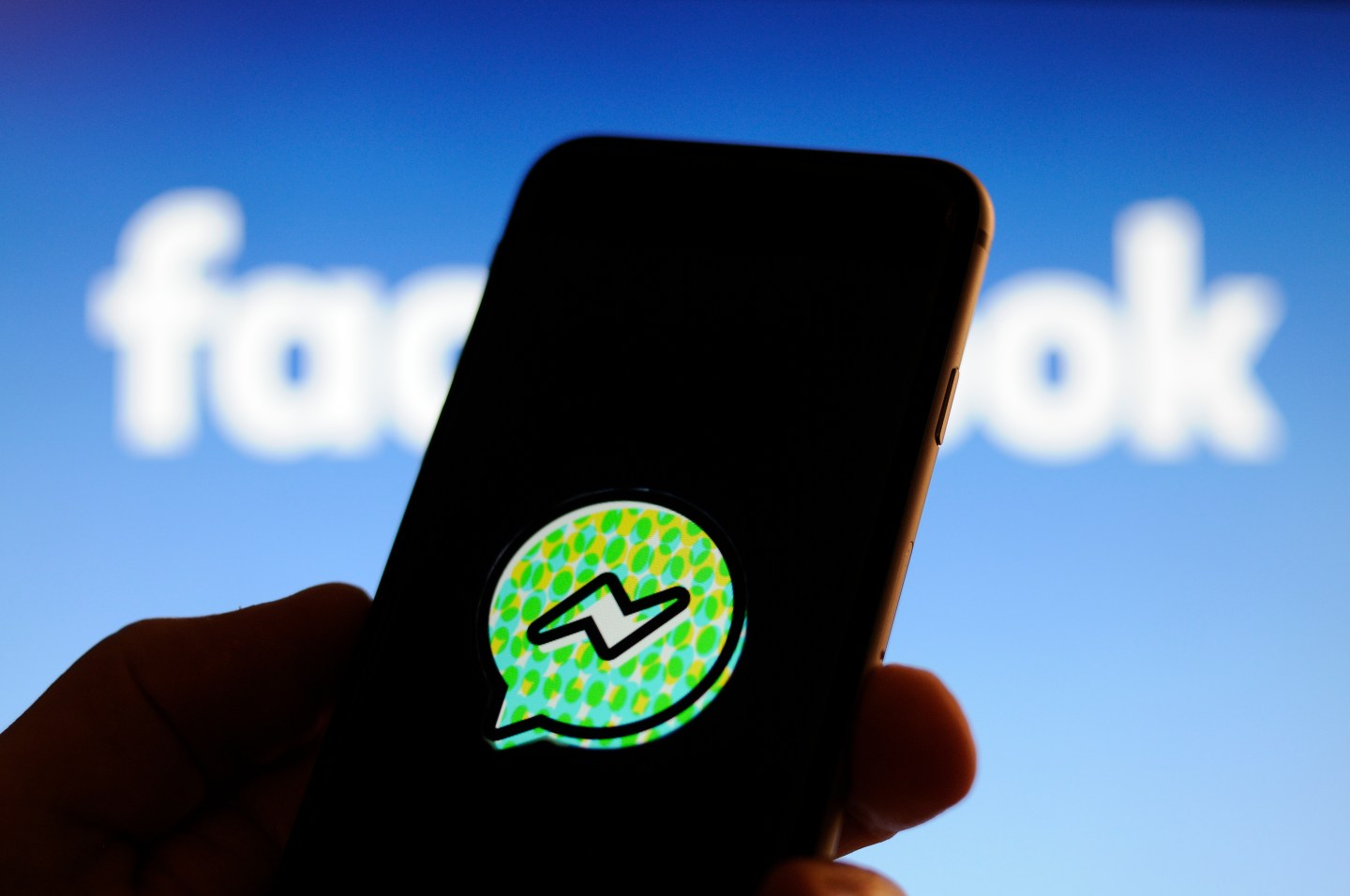A user holds up a smartphone with the Facebook Messenger Kids application logo.