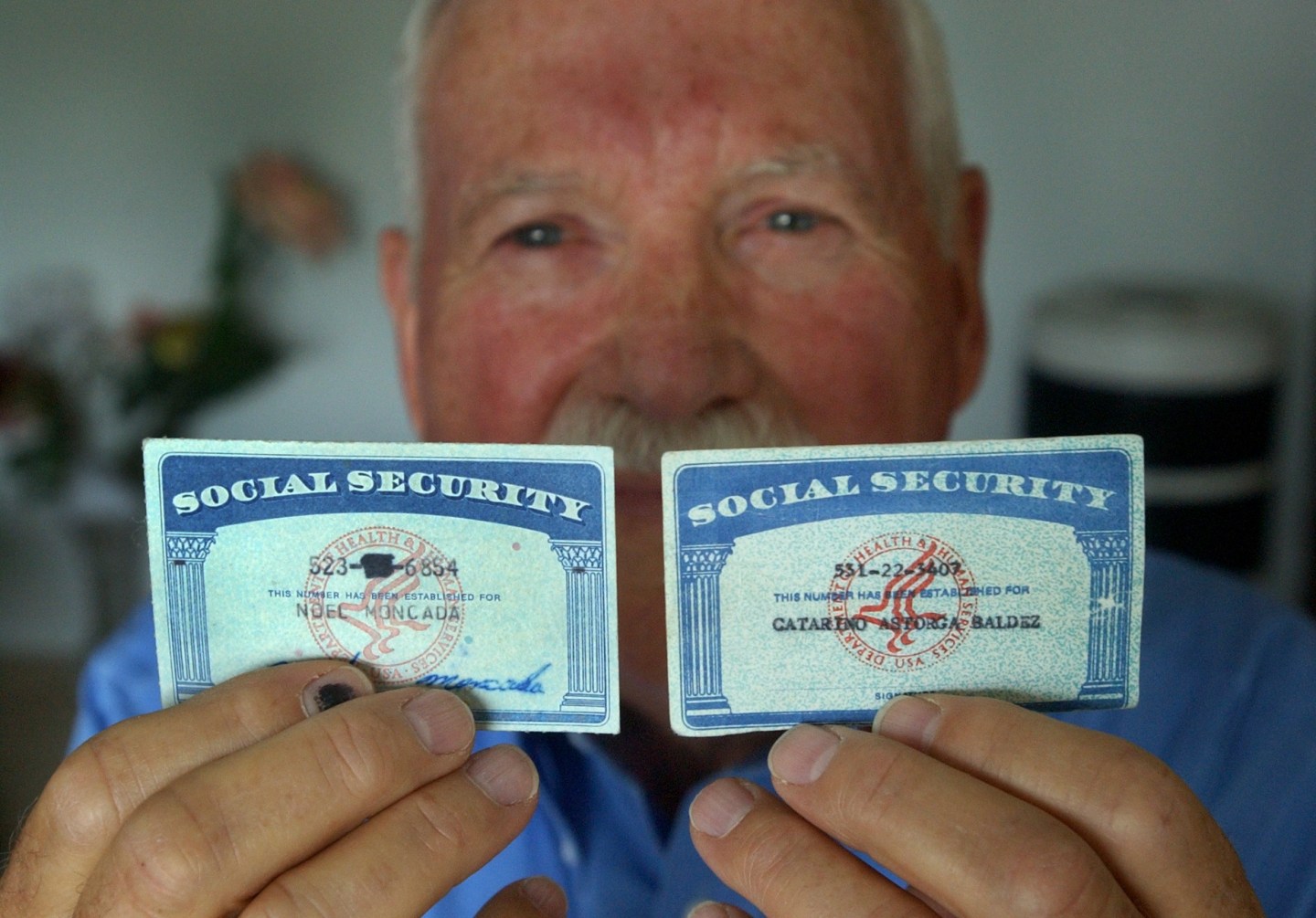A man holds up two social security cards, one real and one fake.