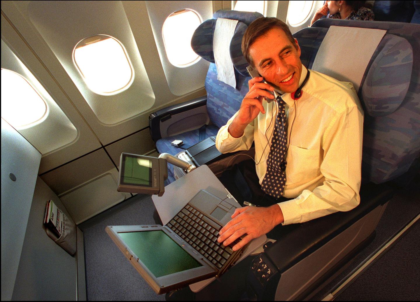 Airline passenger talks on block cell phones with bulky laptop