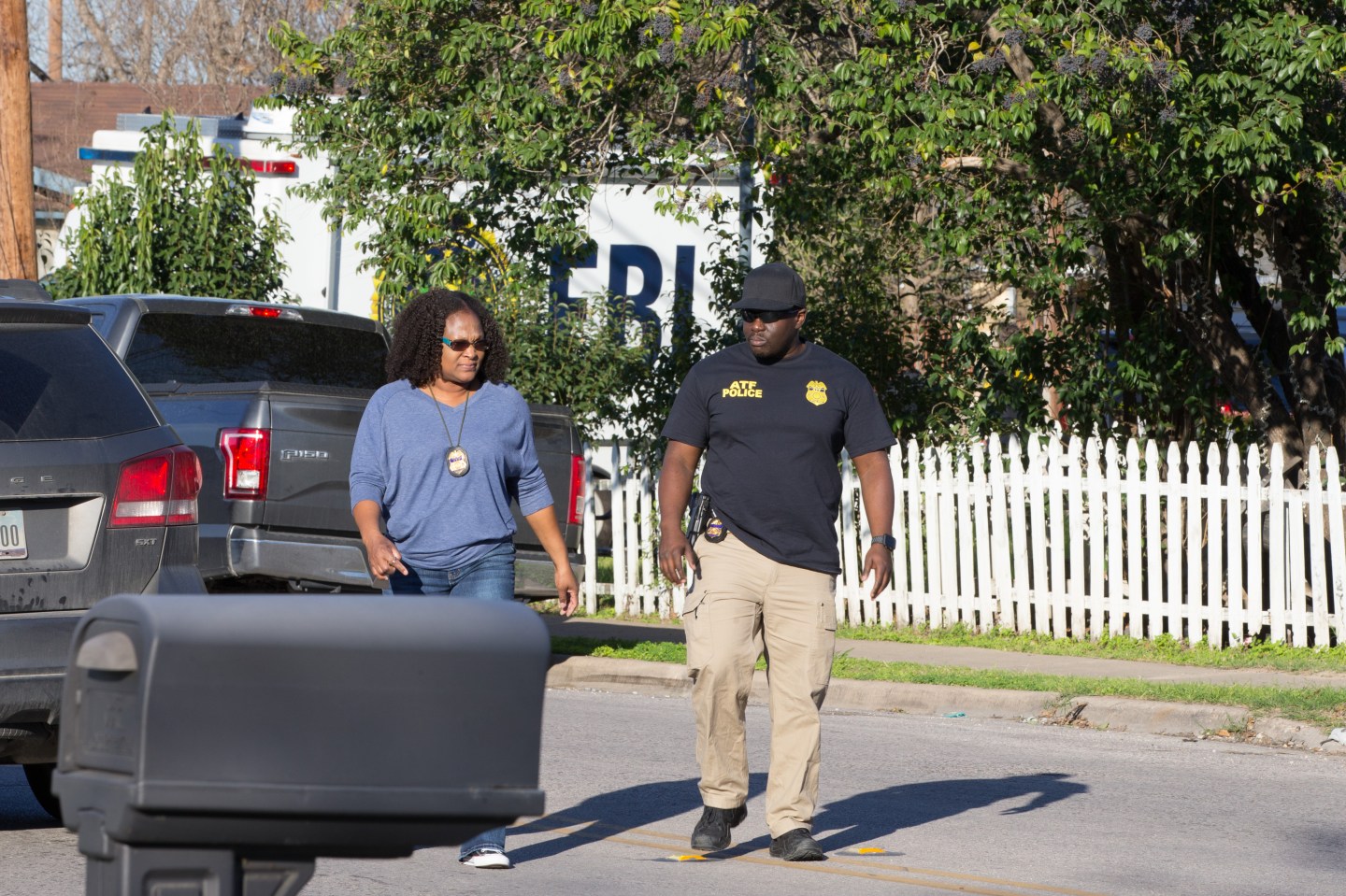 two federal investigators walk away from a vehicle and toward the mailbox of a residence
