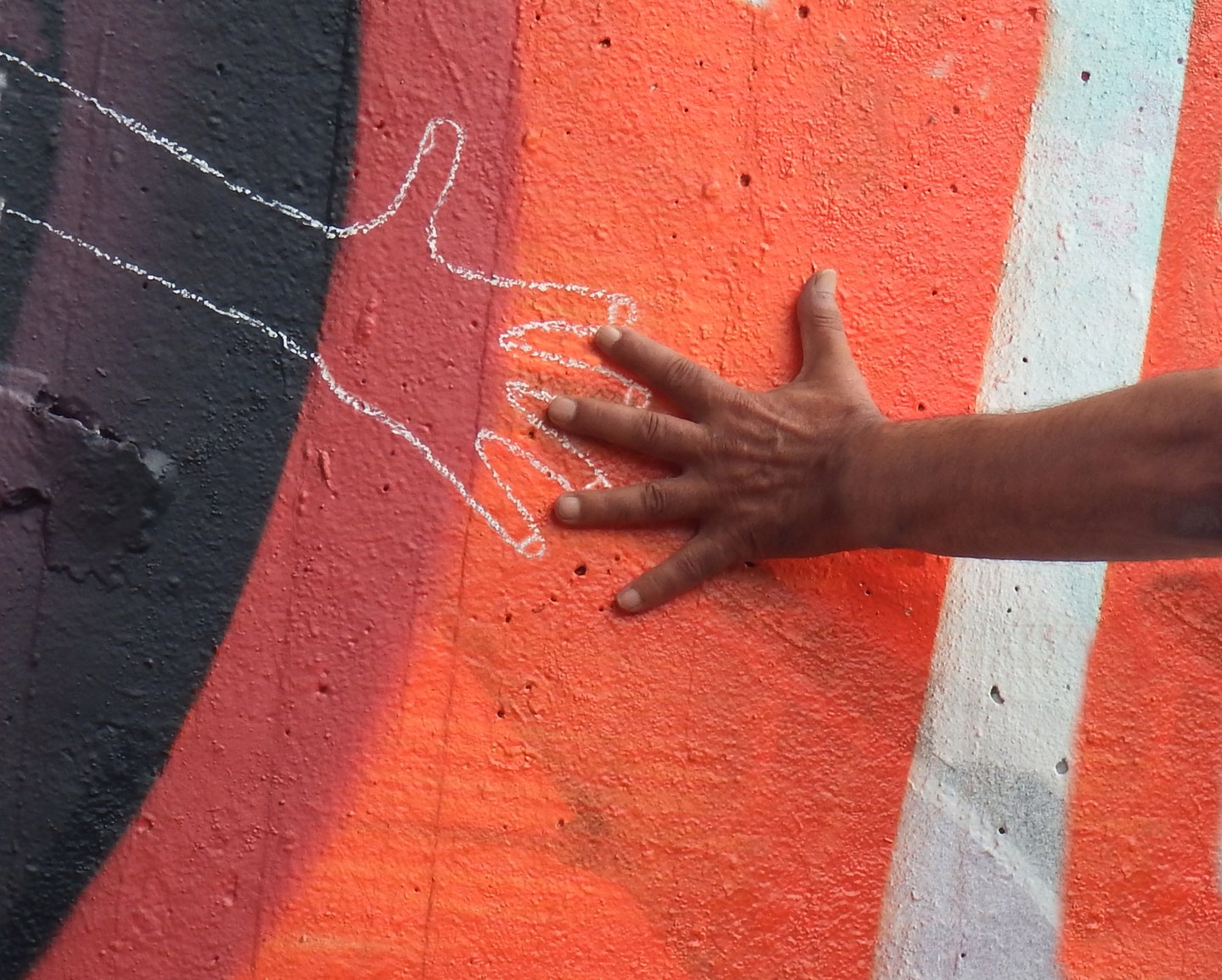 A person's hand reaches out toward a chalk hand drawn on an orange wall.