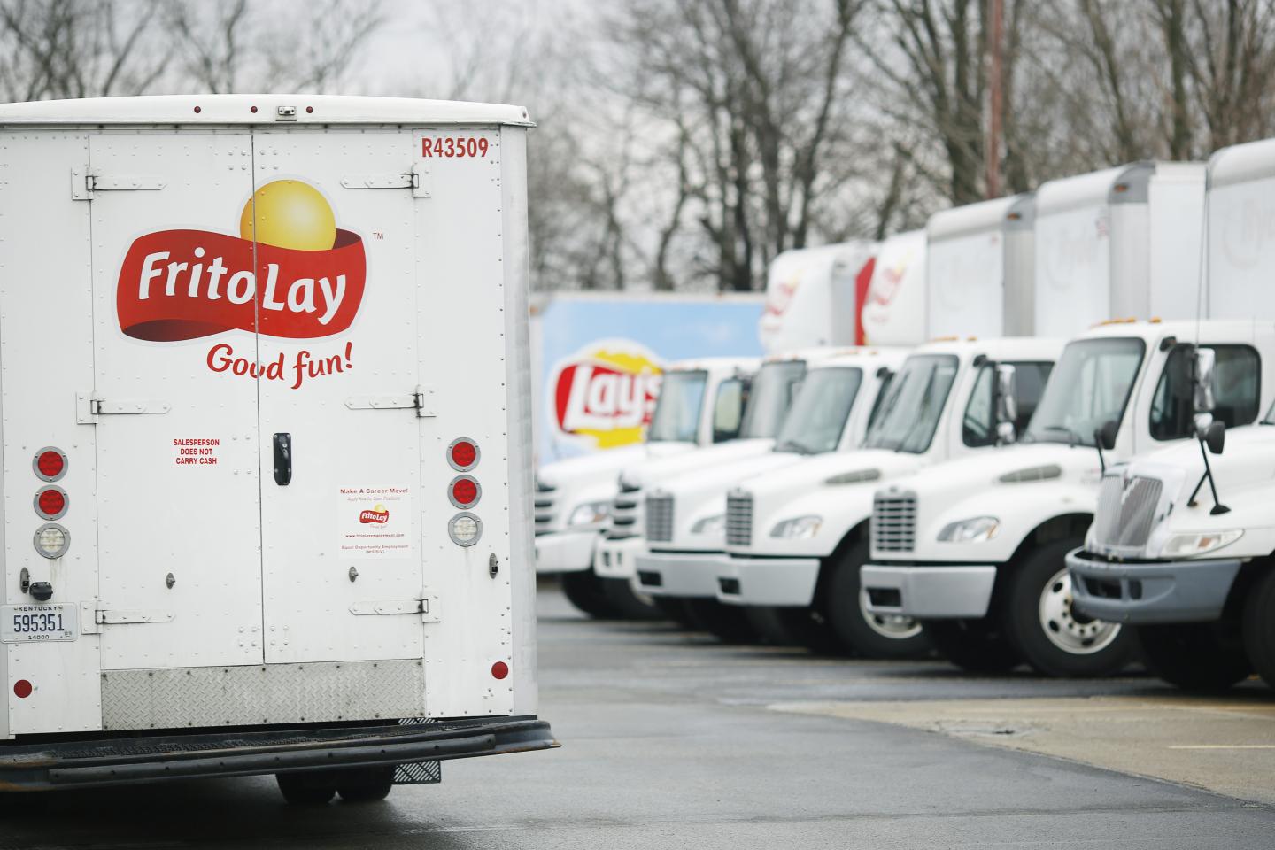 Delivery trucks with PepsiCo Inc. Frito Lay branding sit parked outside a distribution facility
