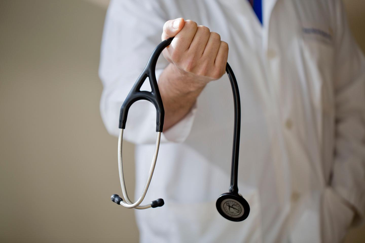 Doctor in white lab coat grips stethoscope