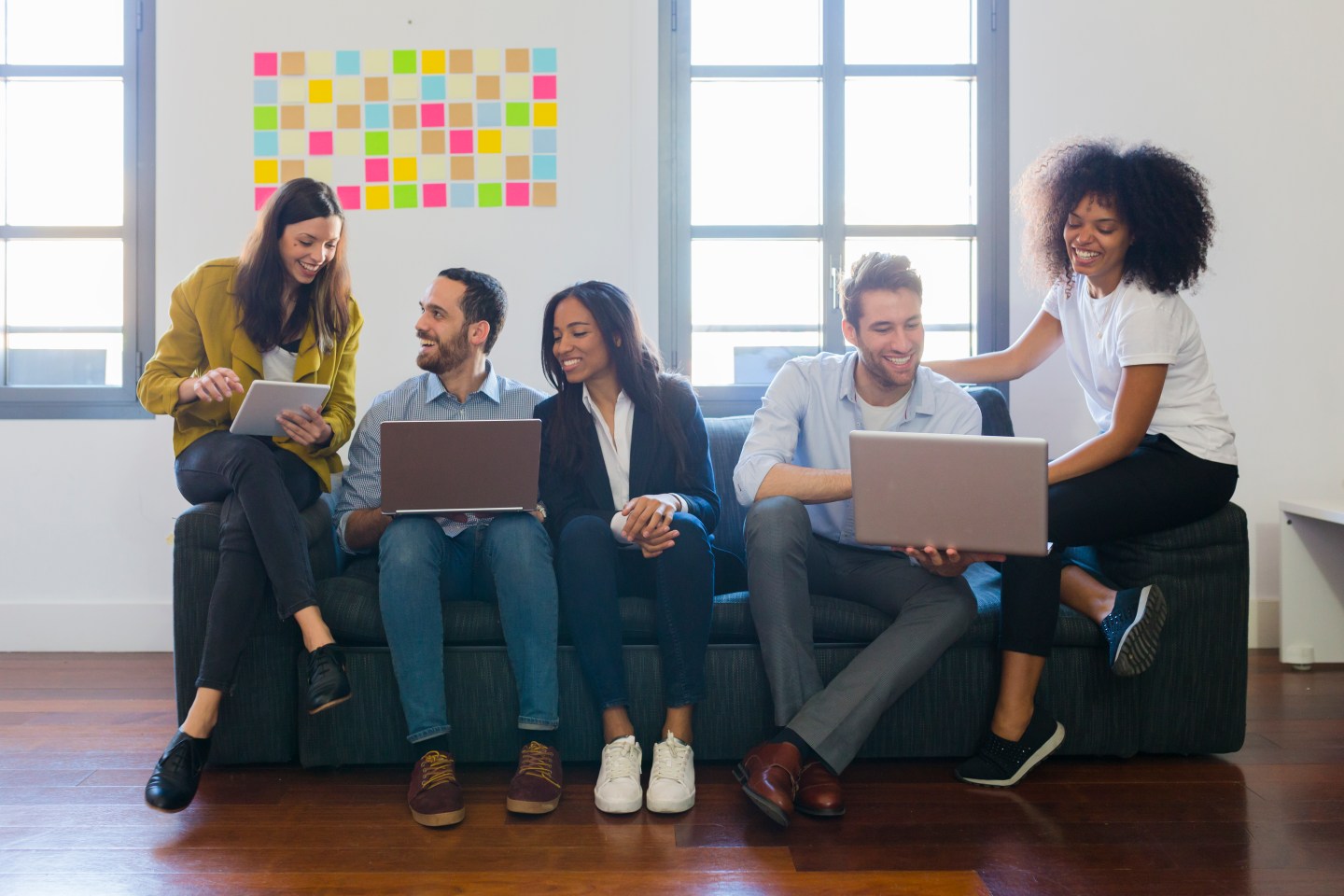 Happy colleagues sitting on couch using laptops