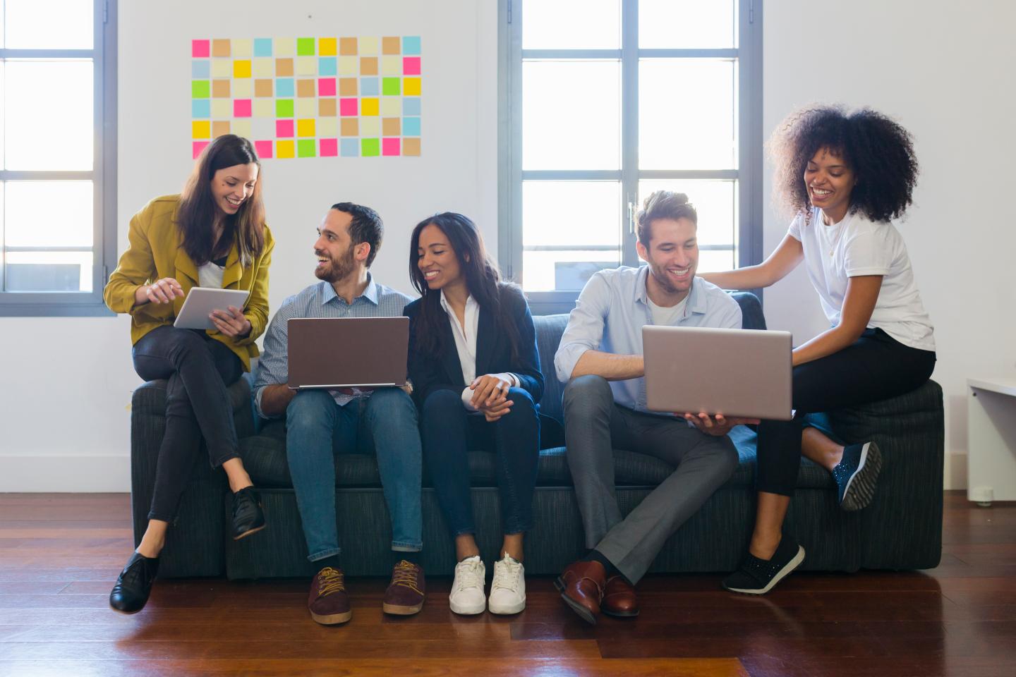 Happy colleagues sitting on couch using laptops