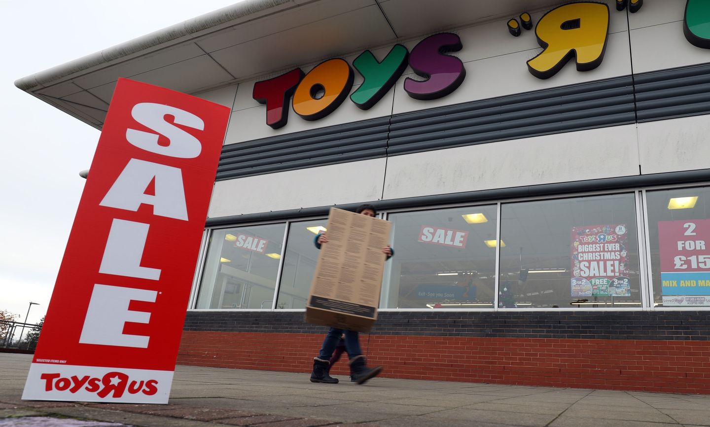 Man carries box outside Toys R Us store that's having a sale
