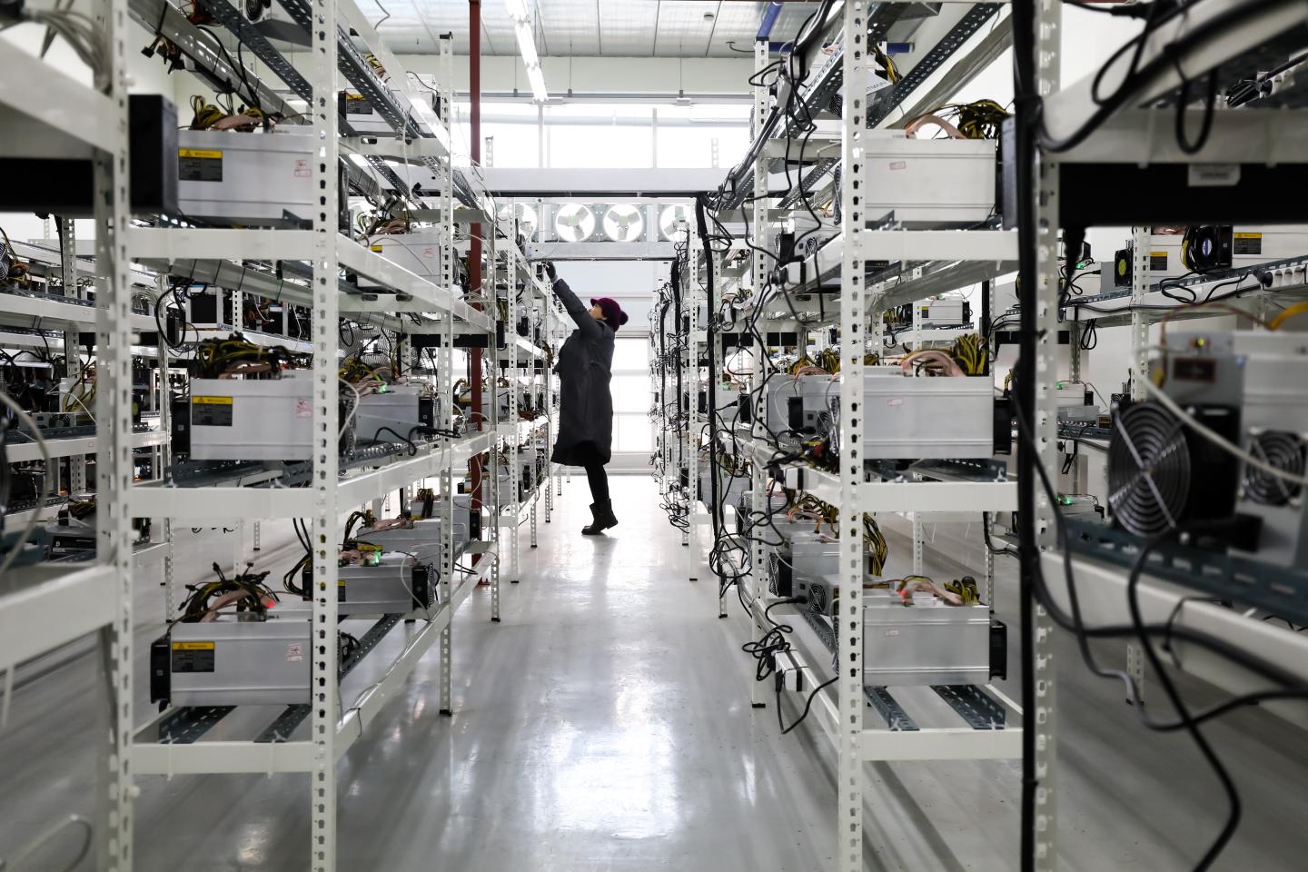 Woman inspects application-specific integrated circuit (ASIC) devices and power units, manufactured by Bitmain Technologies Inc., at her cryptocurrency mining facility