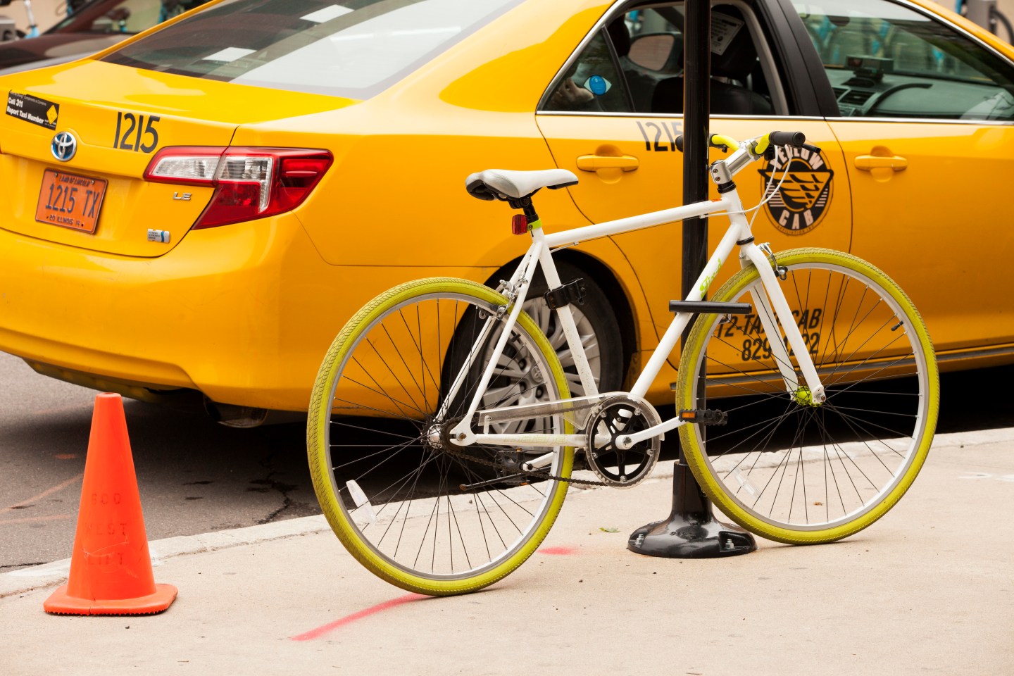 A green bicycle is locked to a pole beside a bright yellow taxi, on June 11, 2014 in Chicago, Illinois.