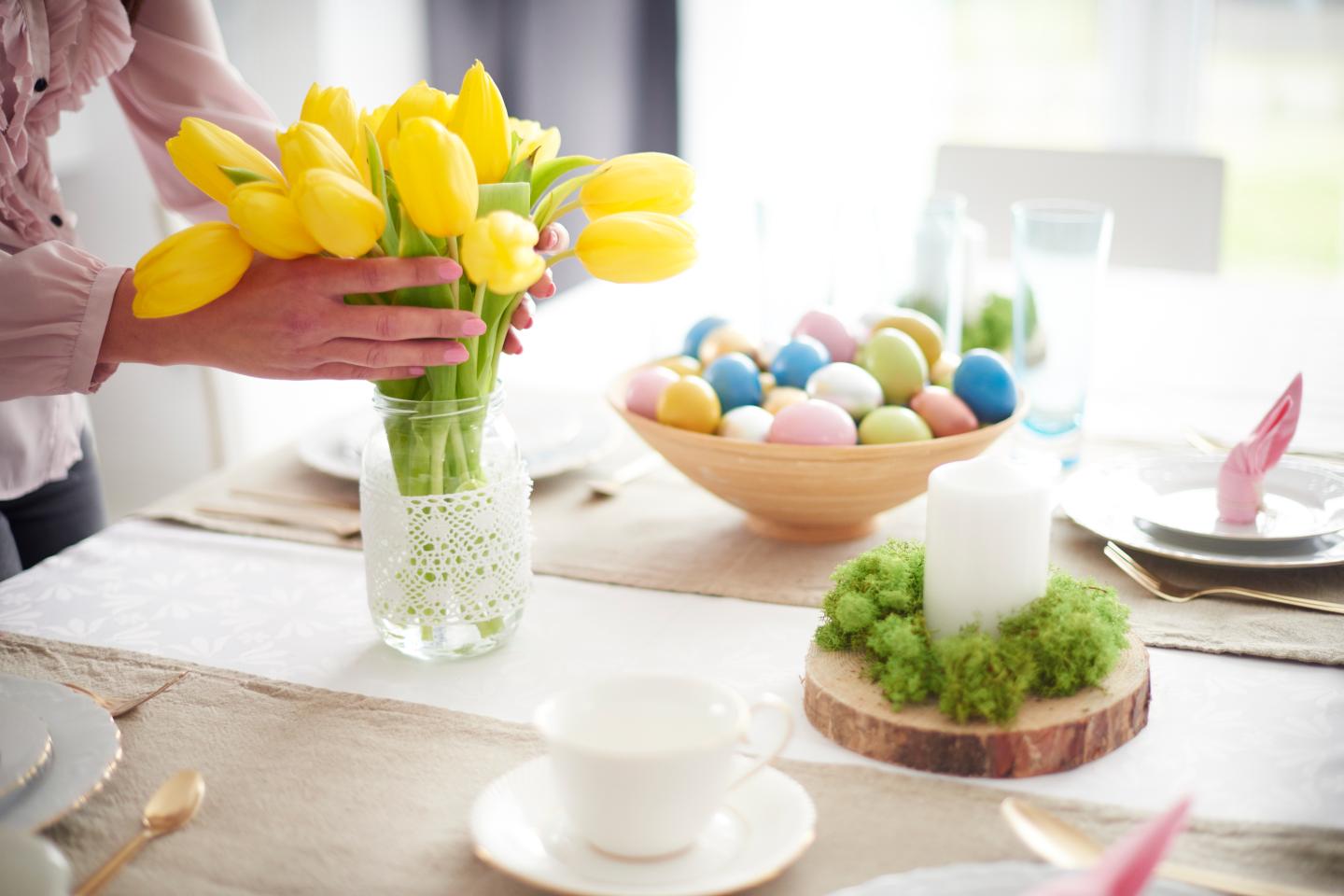 Hands of woman arranging yellow tulips at easter dining table
