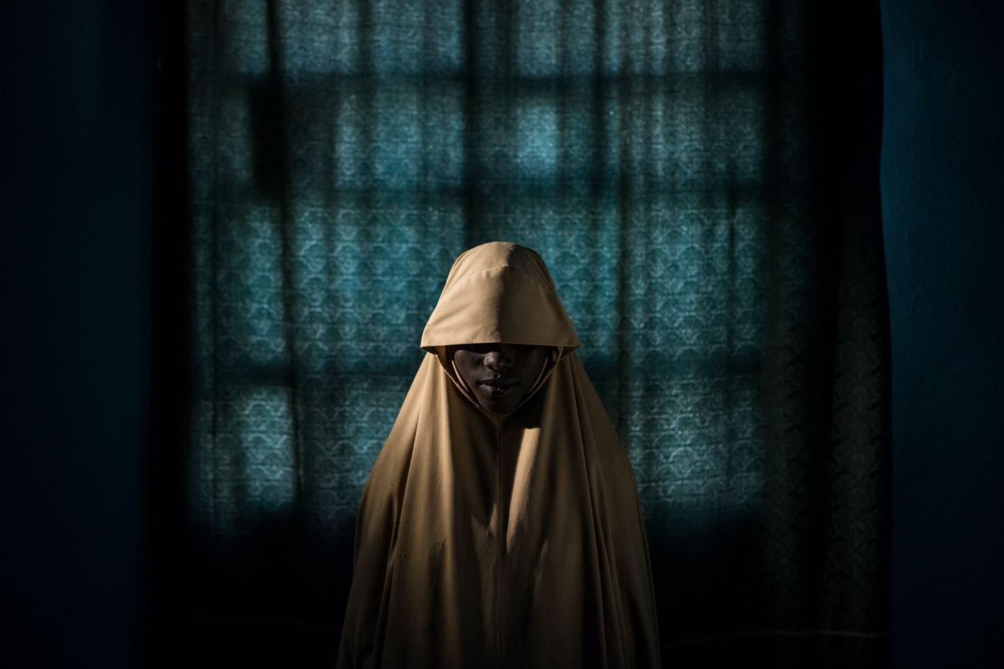 Aisha, age 14, stands for a portrait in Maiduguri, Borno State, Nigeria on Sept. 21, 2017. Aisha was kidnapped by Boko Haram then assigned a suicide bombing mission. After she was strapped with explosives, she found help instead of blowing herself and others up. Photo by Adam Ferguson for The New York Times
