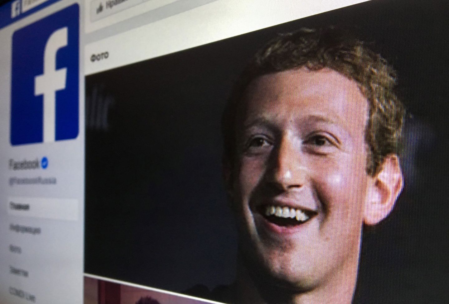 A photo of a computer screen shows Mark Zuckerberg smiling out from a Facebook page's cover photo