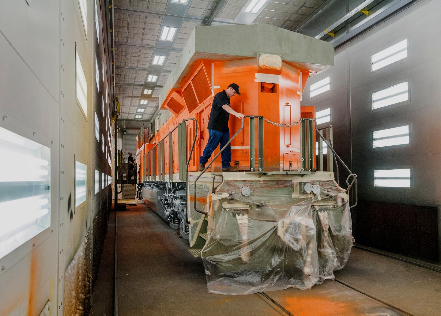 A man works on a bright orange diesel locomotive at a GE facility.