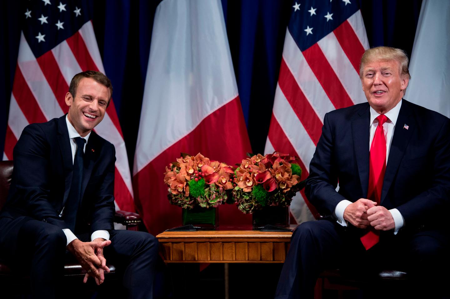 Emmanuel Macron and Donald Trump laugh as they sit next to one another.