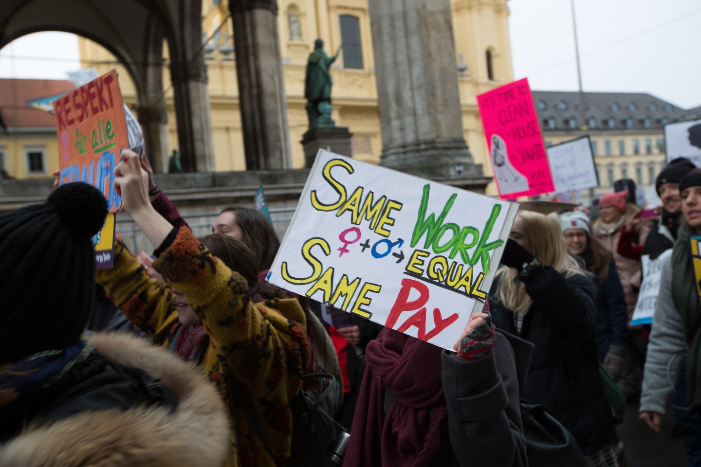 Women hold signs calling for equal pay during a march against Donald Trump in Munich