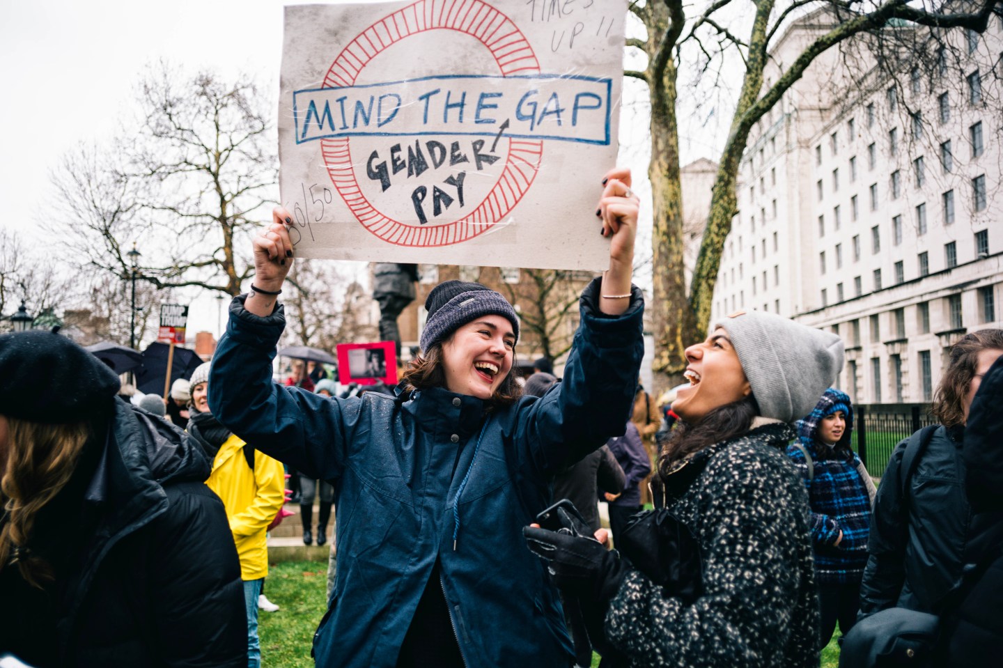 Two women seen laughing while holding a placard during the